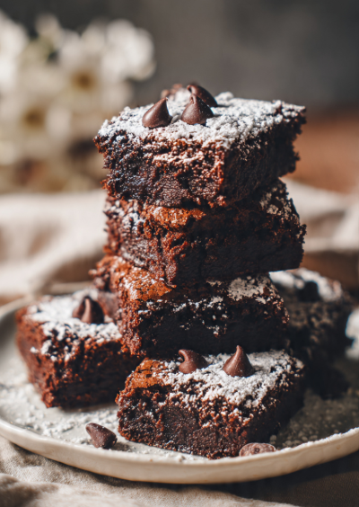Plate of stacked eggless brownies dusted with powdered sugar