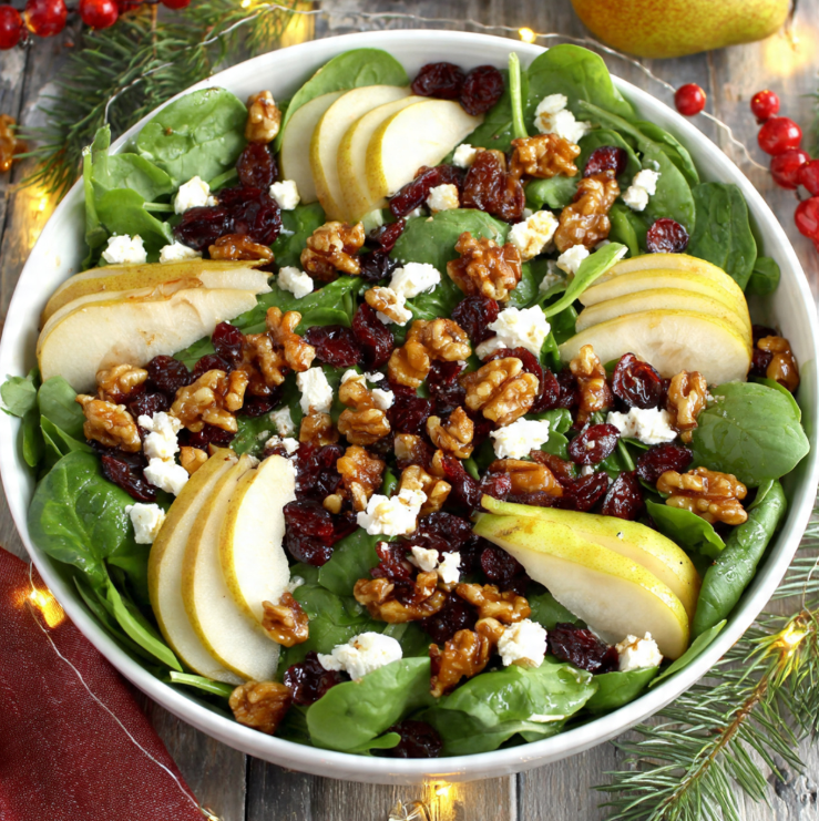 Colorful Christmas salad with mixed greens, dried cranberries, candied walnuts, goat cheese, and sliced pears in a white bowl on a festive holiday table