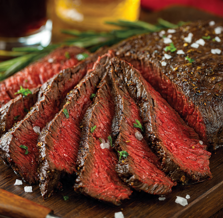 Sliced boneless tri tip steak showing pink center with crusty exterior on wooden cutting board garnished with rosemary and coarse salt
